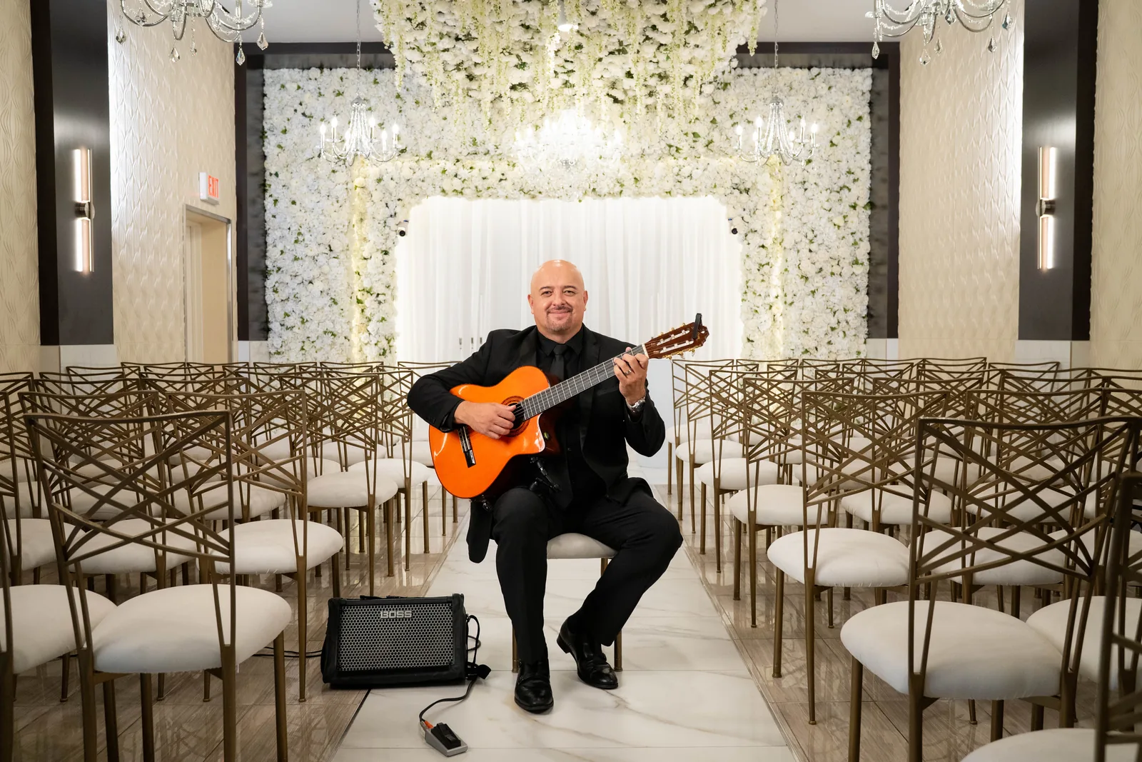 Hans seated in the chapel aisle, smiling with his orange classical guitar