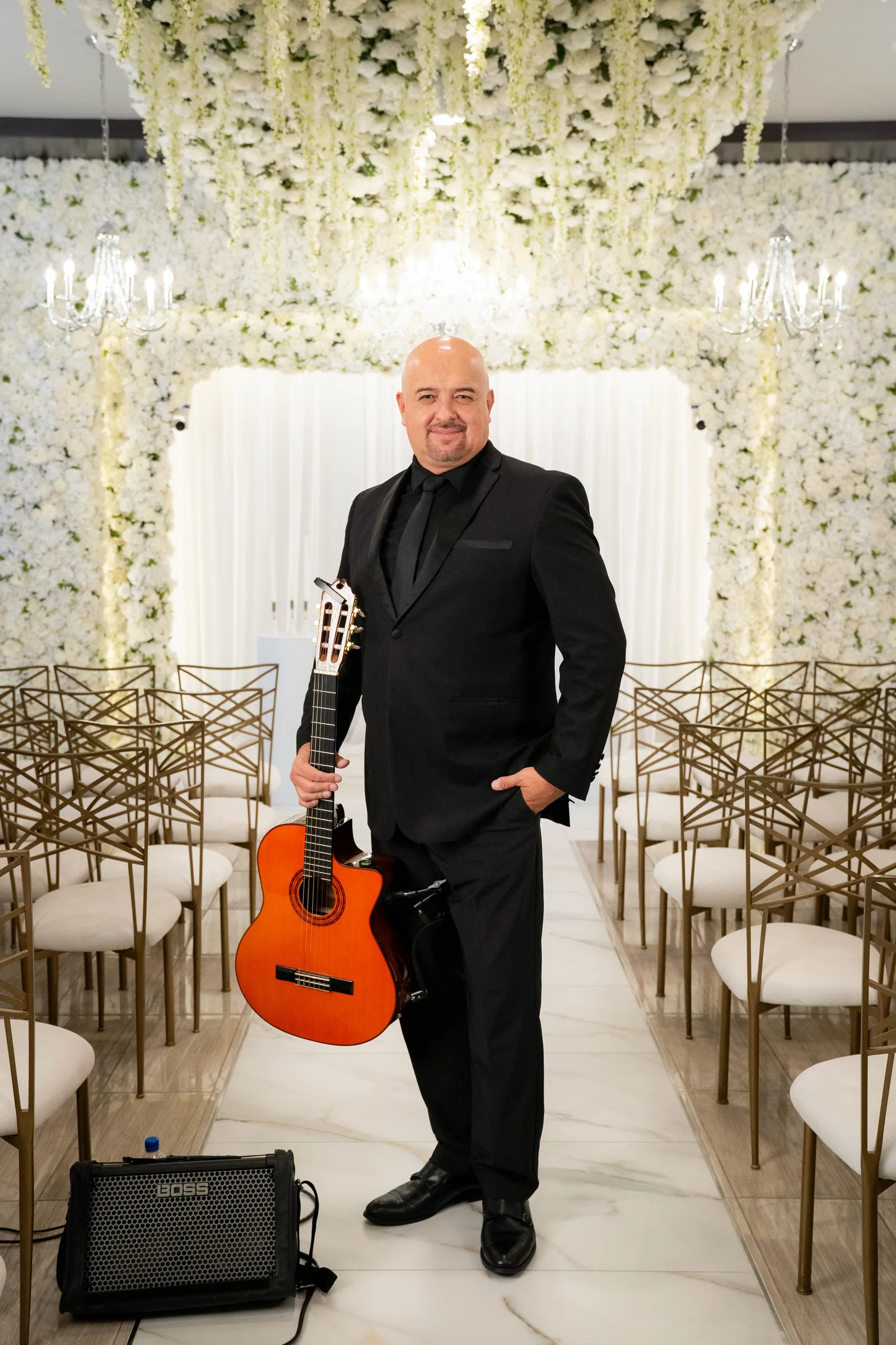 Hans standing in the floral chapel aisle, holding his guitar at his side